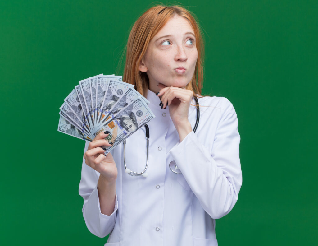 doubtful-young-female-ginger-doctor-wearing-medical-robe-stethoscope-holding-money-touching-chin-looking-side-1024x791 🧠 The Psychology of Money: 7 Habits That Separate the Rich from the Broke