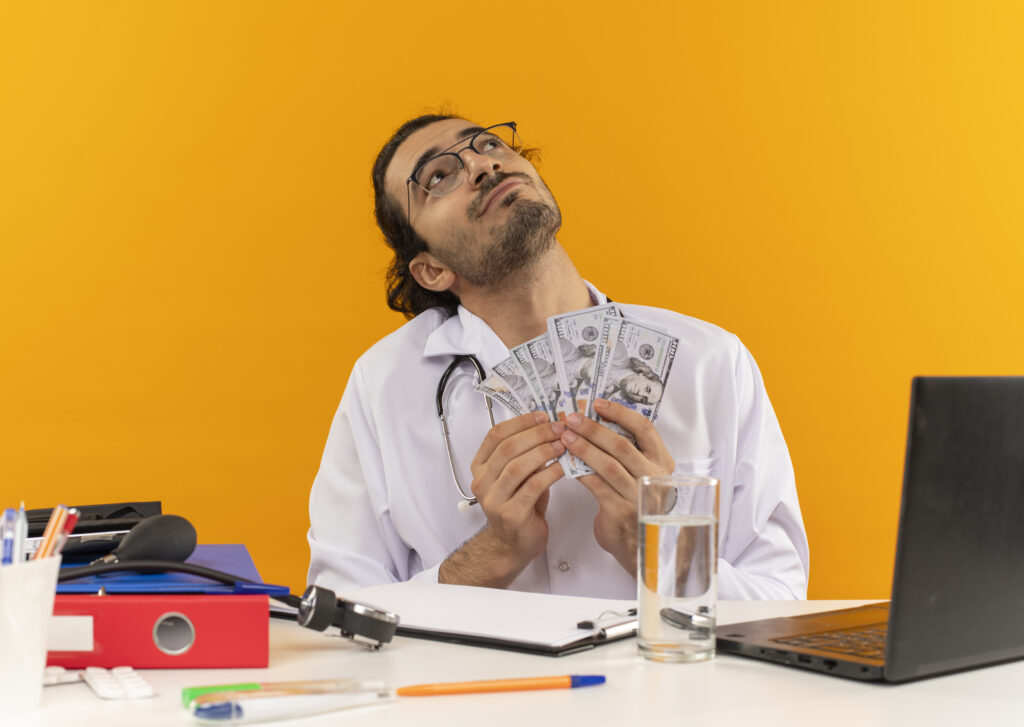 looking-up-pleased-young-male-doctor-with-medical-glasses-wearing-medical-robe-with-stethoscope-sitting-desk-1024x727 🧠 The Psychology of Money: 7 Habits That Separate the Rich from the Broke